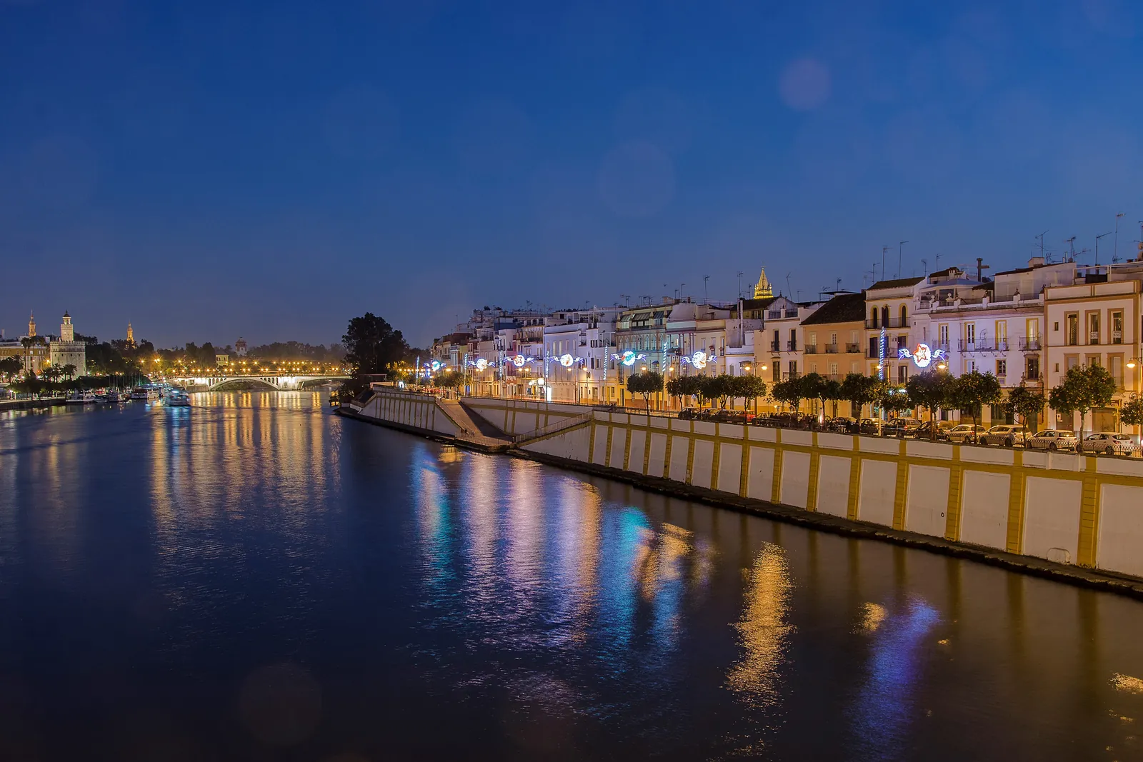 The Guadalquivir at night with the lit houses of Calle Betis reflected in the water and the skyline of Seville in the distance